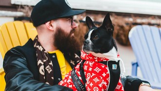 Homem e seu cachorro usam peças do trabalho conjunto entre as marcas Supreme e Louis Vuitton. Em 2017, as duas marcas lançaram uma coleção cápsula que combinava o estilo urbano da Supreme com a sofisticação da Louis Vuitton. As peças, que incluíam desde roupas até acessórios, foram produzidas em quantidades limitadas e rapidamente se tornaram itens de colecionador