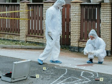Two forensic investigators in white protective suits examine a crime scene with chalk outlines and evidence markers, embodying the real-life horrors that true crime media often dramatizes