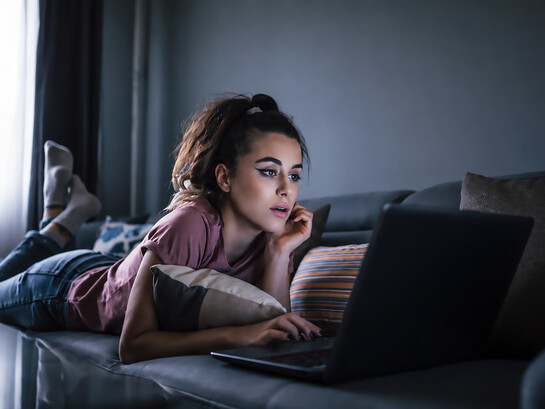 Woman relaxing on the couch while choosing a movie to stream and binge-watch at home