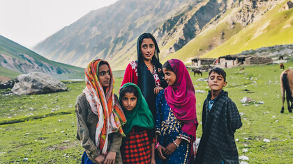A young woman stands on a green grass field under daylight in Kashmir, India
