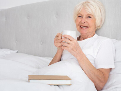 An elderly woman reading and enjoying a cup of tea in her bedroom