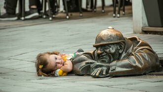 A little girl lies on the street beside a statue in Bratislava, Slovakia