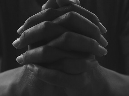 Inside the church, a man bows his head in prayer, his hands folded in deep reverence