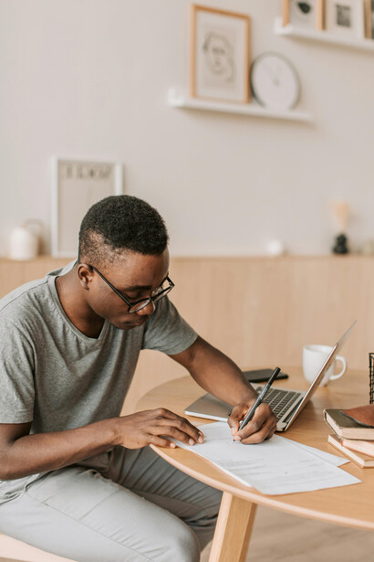 A man in a gray shirt uses a laptop for academic writing