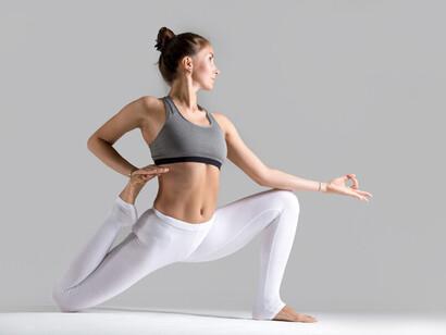 A young woman performing the Eka Pada Rajakapotasana pose against a grey studio background