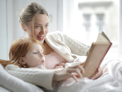 A mother and daughter read a book together in bed, sharing a quiet and engaging moment