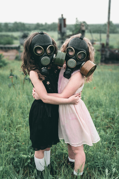 Children wearing gas masks sit together on the grass near a radioactive forest