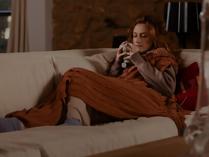 Nestled in winter's embrace, a woman adorned in cozy attire enjoys a sip from her cup, seated comfortably on a couch