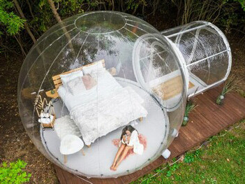 A woman enjoying her stay in a transparent bubble tent at a glamping site, surrounded by geodesic domes at eco-friendly hotels