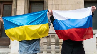 Due mani che reggono due bandiere che non si guardano mai davvero. L’azzurro e il giallo dell’Ucraina tremano nell’aria come un respiro trattenuto; il bianco, il blu e il rosso della Russia pesano come una memoria che non trova pace. Tra i due c’è uno spazio invisibile, carico di storia, di dolore e di parole non dette. Le bandiere sono ferite aperte e identità che si cercano e si respingono. Eppure, nelle mani che le sorreggono, resta un gesto umano, fragile e potente