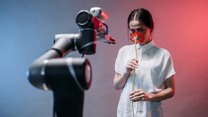 A woman delicately cradles a vibrant red flower while accompanied by an AI-driven robot