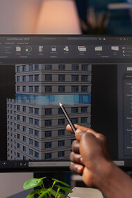 An architect engineer analyzing a construction model on a computer, pointing at an architectural building prototype