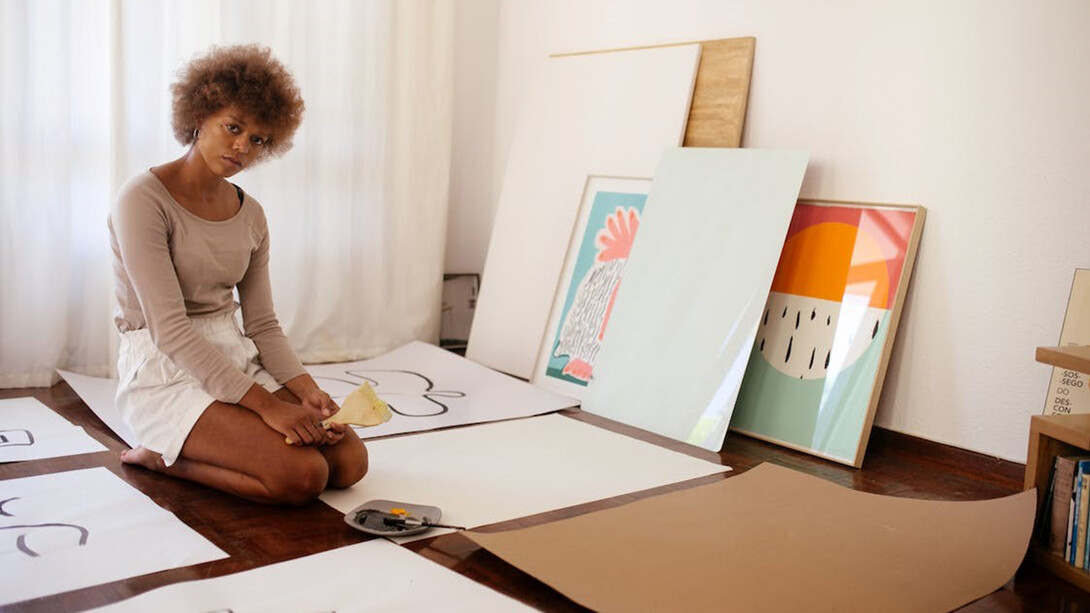 A young artist sitting on the floor surrounded by their artworks