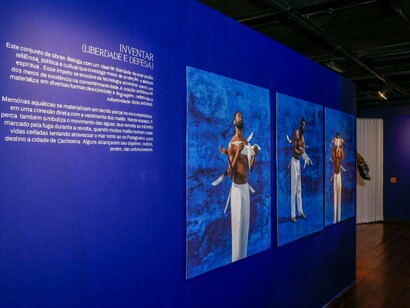 Obras da exposição Ecos Malês ocupam uma das paredes da Casa das Histórias de Salvador, em composição marcada pelo azul e por figuras humanas em movimento. A mostra recupera diferentes experiências de liberdade e resistência que atravessaram a história da Bahia