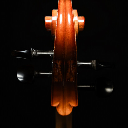 Vista frontal del clavijero y la cabeza tallada de un violonchelo sobre fondo negro