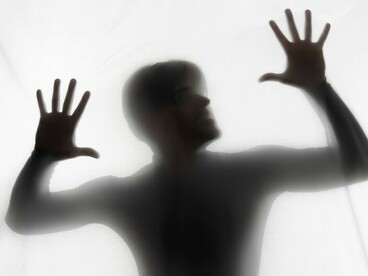 In the studio light, a figure fades into fragments, hands suspended between presence and disappearance