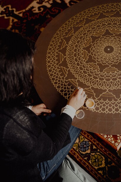 Mulher pinta mandalas douradas em fundo de madeira