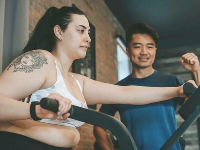 A woman using a machine at the gym to be healthier with the help of a personal trainer