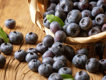 A basket brimming with plump, juicy blueberries rests on a rustic wooden table