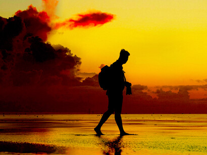 Silhouette of a man walking along the beach at sunset