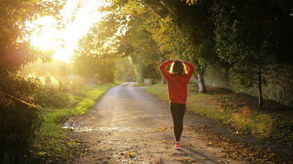 A young woman walking along a sunlit path, setting goals to develop healthier habits