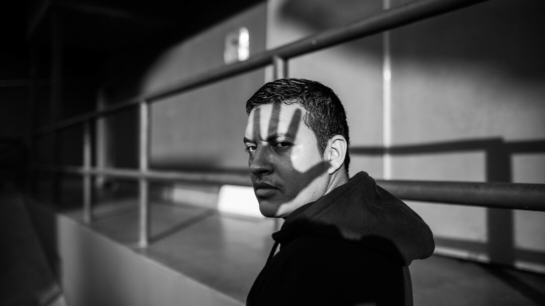 A monochrome photo of a man wearing a hoodie with the shadow of a hand on his face