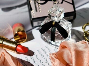 A bottle of perfume and a lipstick are placed on a magazine page