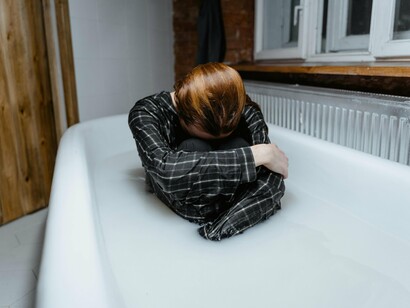 Sitting in a bathtub with knees drawn tightly to the chest, the figure portrays a moment of solitude and emotional weight, shedding light on how the pressure to constantly achieve more can erode mental well-being