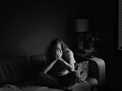 A woman covers her face while sitting on her couch thinking, alone. The low self-esteem of the human species is reflected in its devaluation and self-destruction