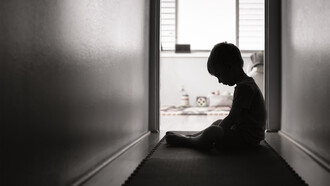 A child sits on the floor, their expression one of sadness and despair