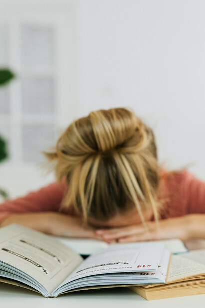 A girl sleeping with her head on open books, an image of fading energy and drift