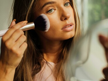 A woman getting ready while holding a makeup brush and mirror