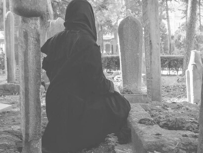 A woman kneeling next to the buried at the cemetery 