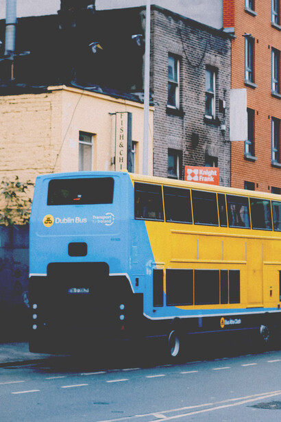A blue-and-yellow old double-decker bus driving along a rain-wet cobblestone street in Dublin, Ireland