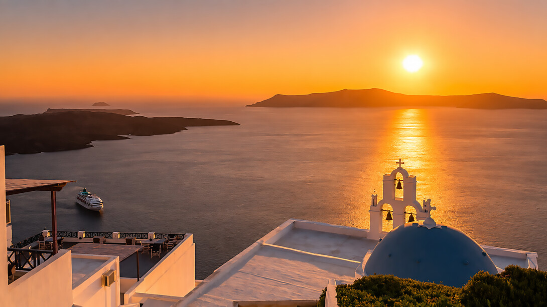 A breathtaking summer sunset over Santorini, Greece, bathing the island's iconic whitewashed buildings in golden light