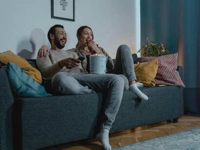 A man and a woman sit on a blue sofa, eating popcorn together