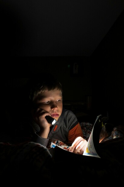 A child reading a comic book in bed, holding a flashlight