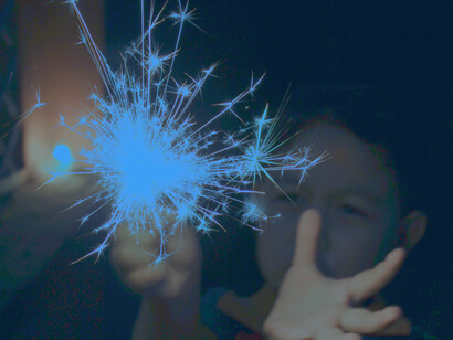A young child holds a sparkler in awe