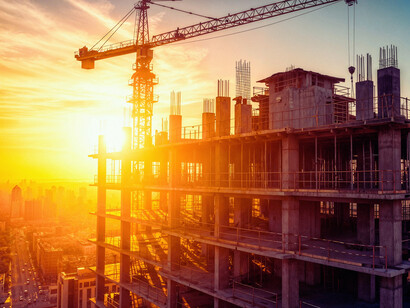 Tower crane rising over an active construction site at dusk, symbolising the bridge between design ambition and site conditions