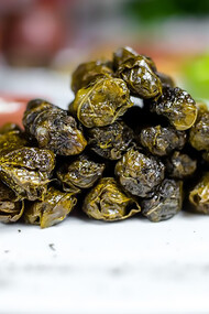 Yaprak sarması features minced meat and spices wrapped in grape leaves, served with plain yogurt, showcasing a classic side of Turkish cuisine