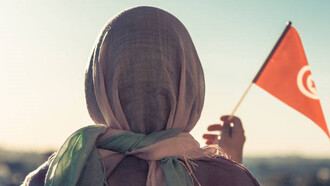 Muslim woman in scarf with Tunisia flag at sunset