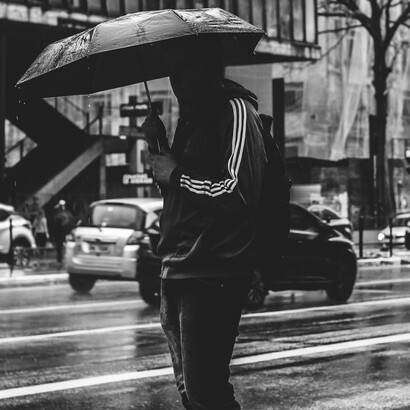 Homem com seu guarda-chuva espera para atravessar e continuar sua trajetória sem rumo por São Paulo, Brasil