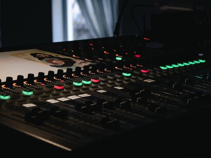 A traditional sound board covered in knobs stands next to a screen displaying an AI-generated composition, merging old-school sound design with cutting-edge technology