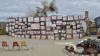 Ell muro de la verdad en Slab City; televisores con palabras de noticias falsas y mensajes de propaganda frente a deshechos electrónicos