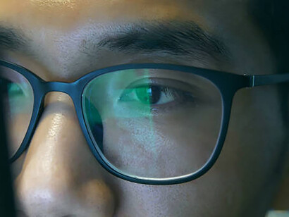 Enveloped by the era of digitalism, a young businessman's intent gaze at a computer screen is mirrored within his glasses, encapsulating the pervasive nature of technology's influence across all spheres of life