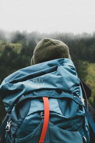A lone backpacker stands still overlooking a vast landscape, taking in the distance not as a destination to conquer but as a moment to fully experience and carry forward