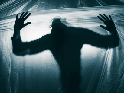 Silhouetted against a translucent barrier, a figure presses forward, hands outstretched, symbolizing a struggle against an unseen force, evoking themes of isolation and otherness