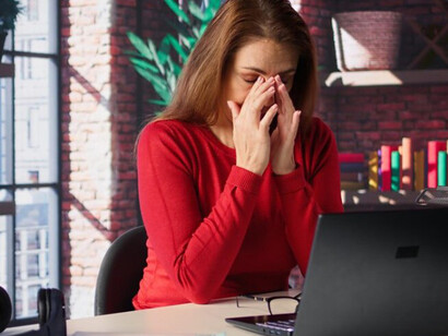 A tired, burned-out woman sits at her desk in her loft, staring at her laptop screen as she yawns