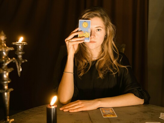 Uma mulher observa atentamente cartas dispostas sobre a mesa durante uma leitura de tarot. Entre símbolos e interpretações, o artigo convida a refletir sobre como práticas voltadas ao autoconhecimento podem ampliar a compreensão de si, mas também reforçar crenças limitantes quando passam a orientar decisões de forma acrítica