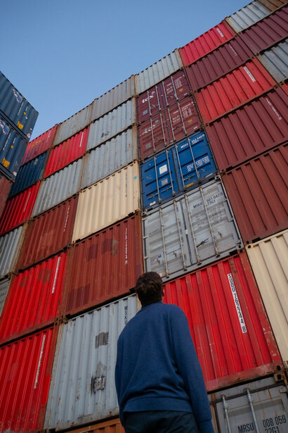 Man in black jacket standing in front of red and blue intermodal containers, China
